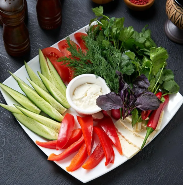 Masa cu legume, frunze verzi și un bol cu mâncare colorată